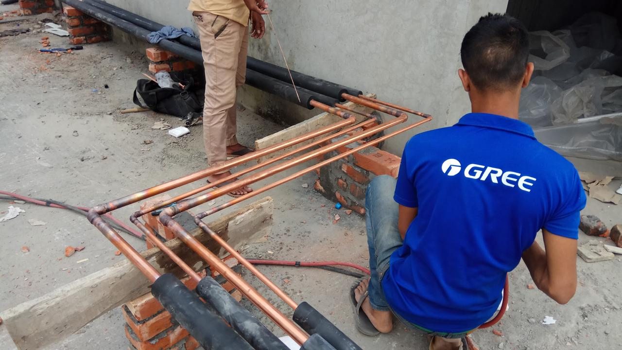 Technician brazing copper refrigerant pipe runs with insulation on a construction site